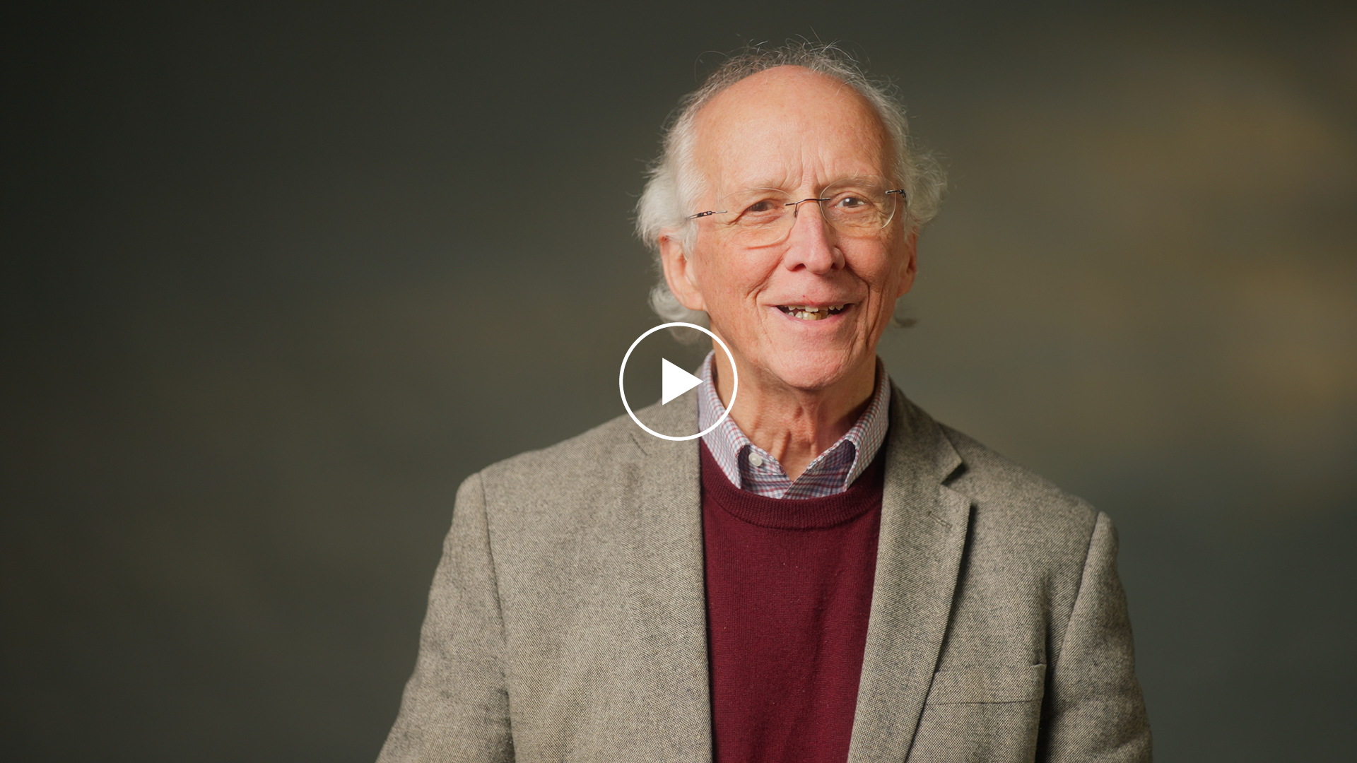A photo of John Piper looking into the camera in front of a brown background.