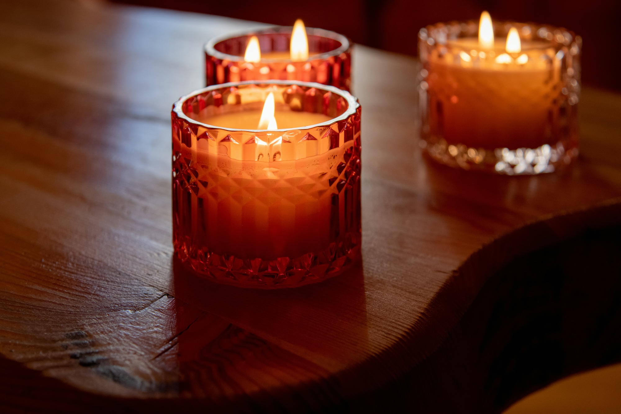 An image of several lit candles in glass holders sitting on a wooden table.