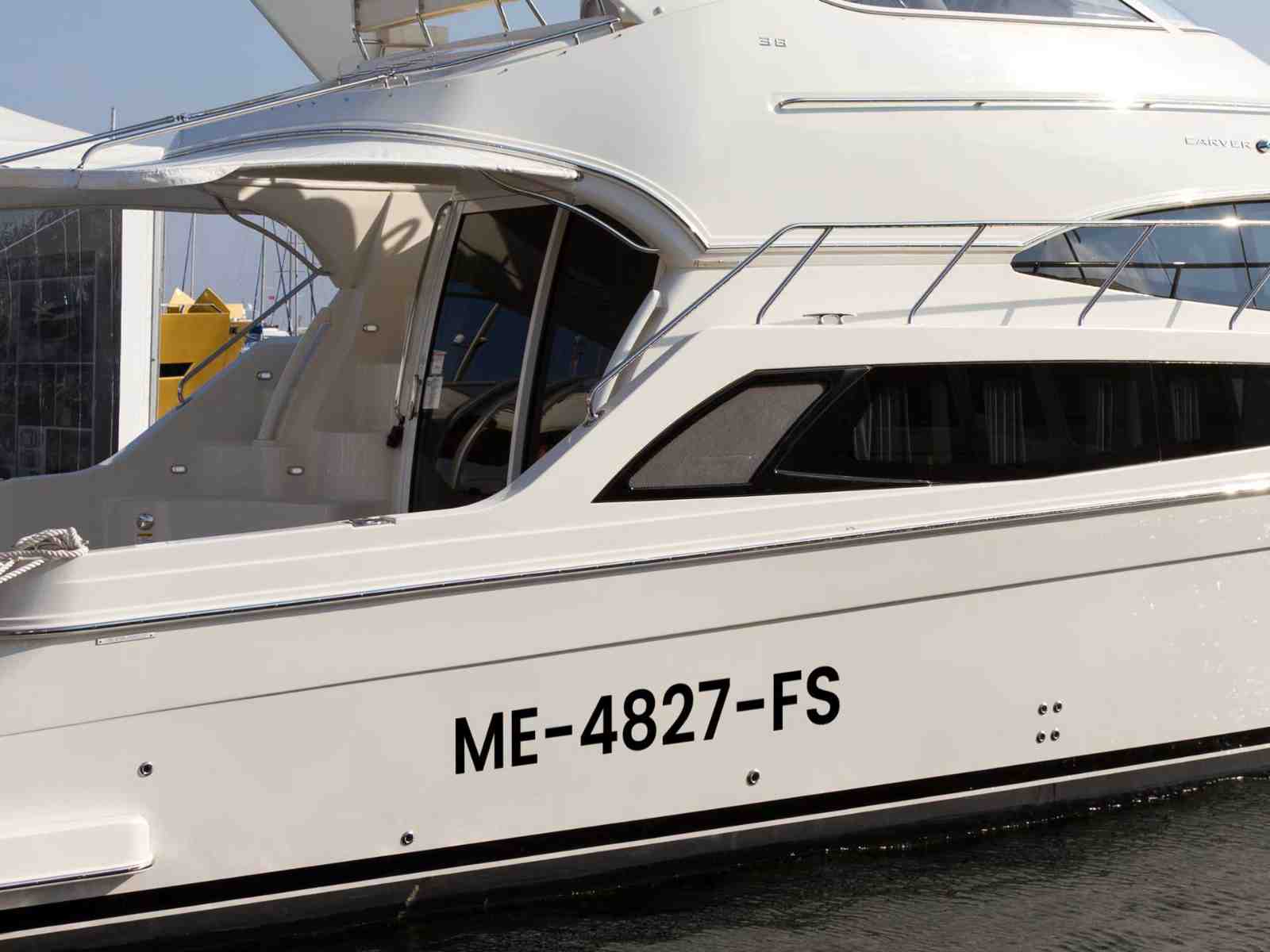 Black boat registration numbers "ME-4827-FS" displayed on the white hull of a docked yacht for vessel identification.
