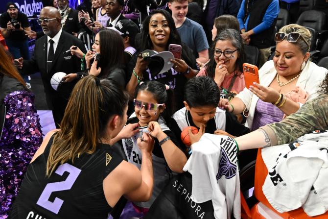 A Golden State Valkyries player signs autographs and greets young fans gathered courtside after a game