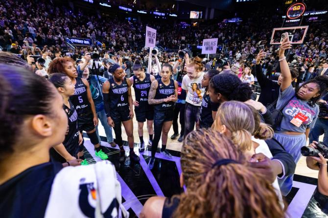 Golden State Valkyries players gather in a postgame huddle on the court as photographers and fans surround them after a win