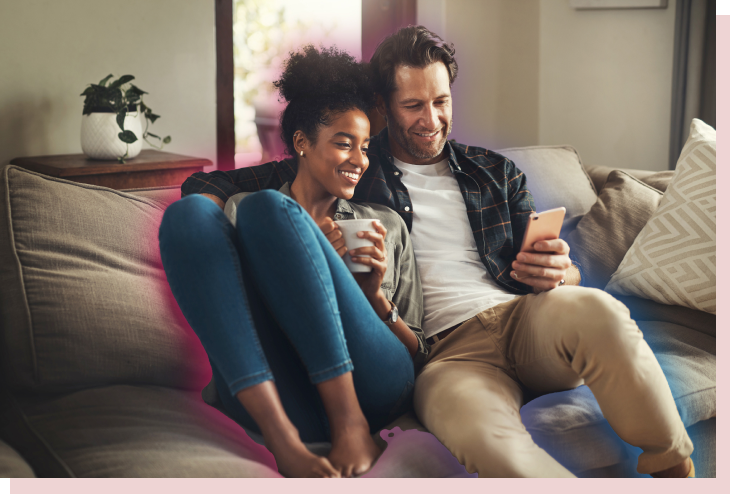 image of a couple sitting on the couch admiring their smart energy savings on their phone