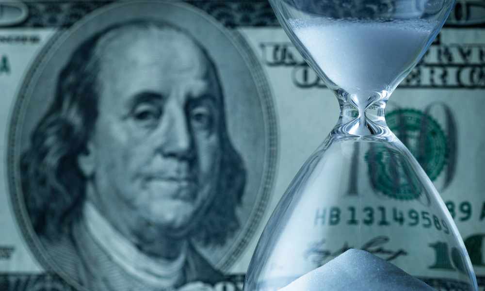 hourglass with sand running down in front of 100-dollar bill