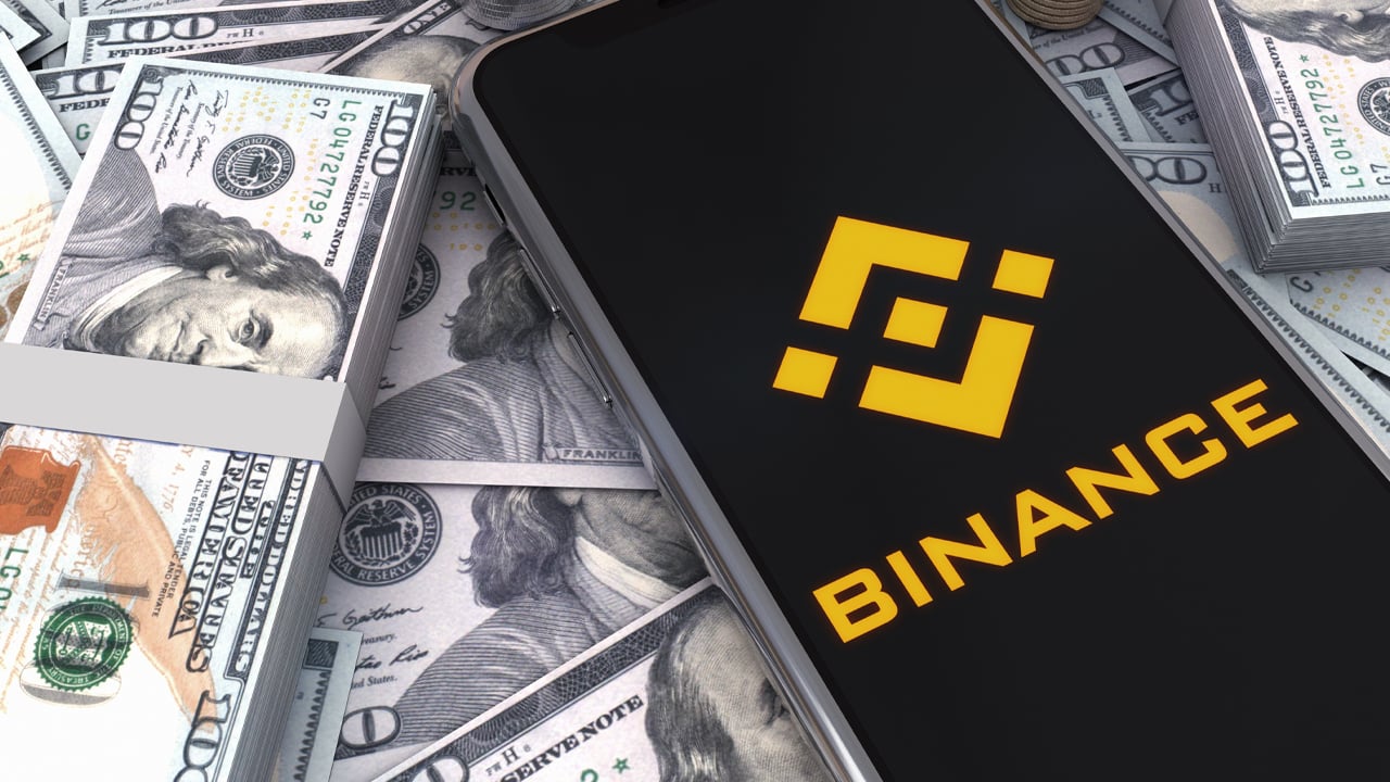 Binance logo on smartphone laying on 100-dollar bills